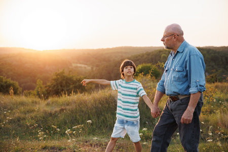 Photo of a little boy with his grandfather walking in a field at summerの写真素材