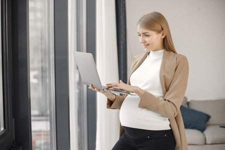 Pregnant lady typing on a laptop while standing in modern officeの写真素材