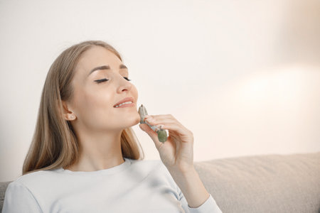 Portrait of woman sitting in living room holding a face massagerの写真素材