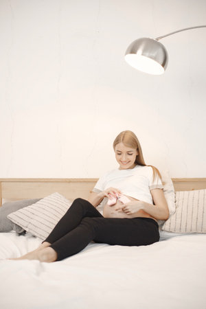 Pregnant lady lie on a bed in room and holding a little baby socksの写真素材