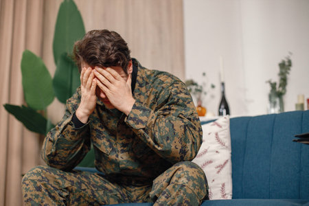 Portrait of young military man sitting on a coach hiding his faceの写真素材