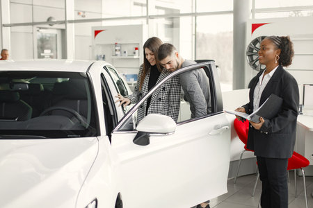 Black saleswoman standing at auto showroom and consulting a young coupleの写真素材