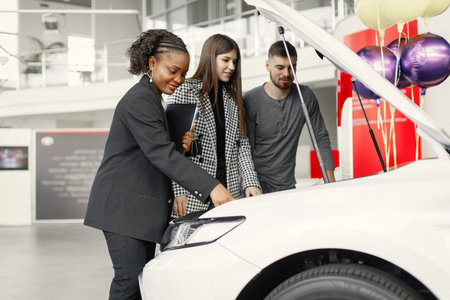 Black saleswoman standing at auto showroom and consulting a young coupleの写真素材