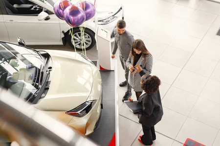 Black saleswoman standing at auto showroom with young coupleの写真素材
