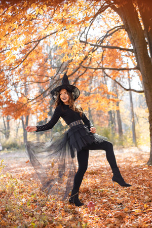 Woman in witch costume standing in autumn forest on Halloween