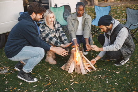 Young friends warming hands by fire at forestの写真素材