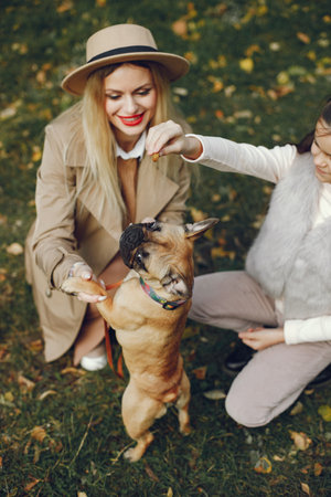 Mother and her daughter with a little puppy french bulldog in a parkの写真素材
