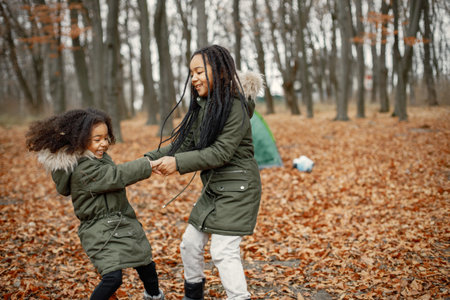 Two little black sisters playing near tent camping in the autumn forestの写真素材