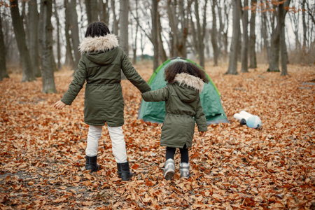 Two little black sisters playing near tent camping in the autumn forestの写真素材