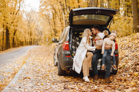 Young family sitting at open trunk of hatchback car in autumn forestの写真素材