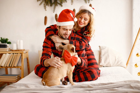 Couple wearing christmas plaid red pajamas with dog on bedの写真素材