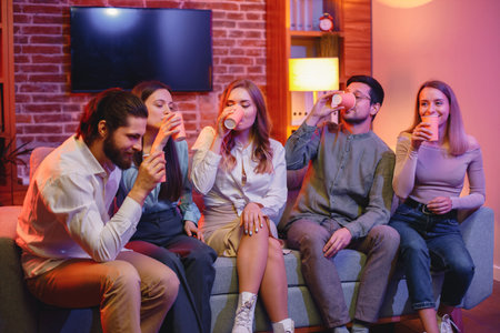 Five friends sitting on a sofa in a cozy room and talking togetherの写真素材