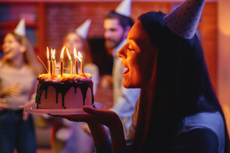 Woman holding a plate with birthday cake in front of blurred people on a partyの写真素材