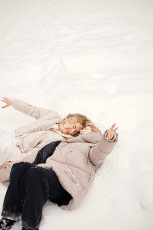 Portrait of blonde mother and teen daughter lay on a snow in winter forestの写真素材