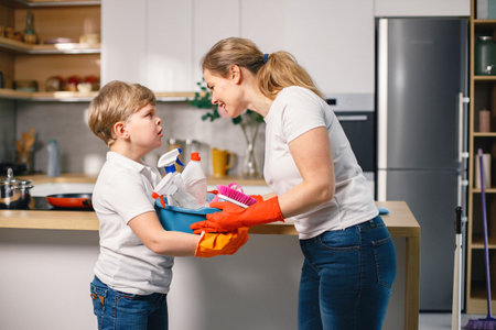 Little boy and his mother cleaning in a kitchen using a detergentsの写真素材