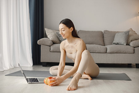 Young fitness woman sitting on yoga mat at home and using a laptopの写真素材