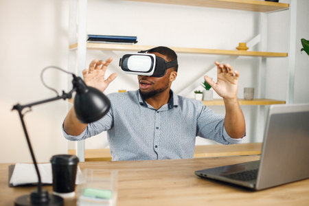 Black male entrepreneur sitting in office and using virtual reality glassesの写真素材