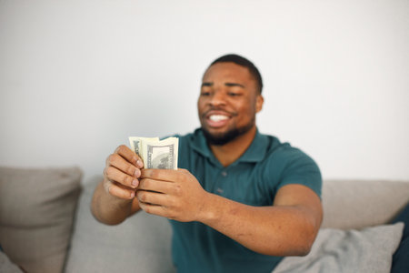 Black guy sitting on a couch in living room holding a cashの写真素材