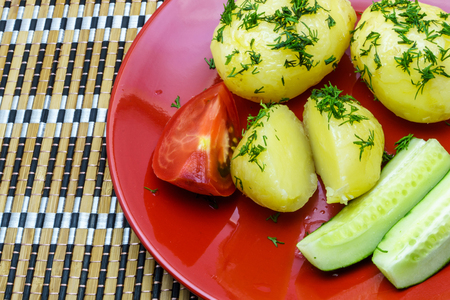 Boiled young potatoes with slices of cucumber and tomato on a plateの写真素材