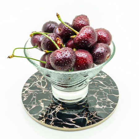Glass vase on a stand with fresh wet cherries isolated on white background