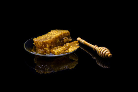 Honey with honeycombs on a glass plate isolated on a black background