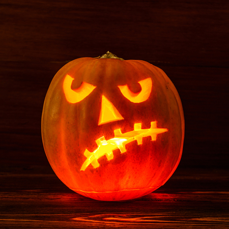 Scary Halloween pumpkin isolated on a wooden background . Scary glowing face trick or treat. Concept of halloween pumpkin on wooden planks.の写真素材