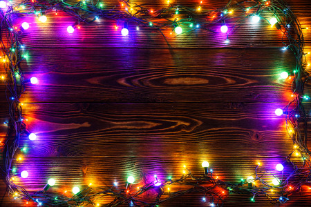 Wreath and garlands of colored light bulbs.Christmas background with lights and free text space. Christmas lights border. Glowing colorful Christmas lights on a wooden background. New Year.の写真素材