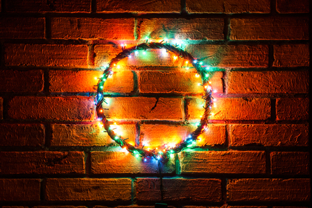 Wreath and garlands of colored light bulbs.Christmas background with lights and free text space. Christmas lights border. Glowing colorful Christmas lights on a brick wall background. New Year.の写真素材