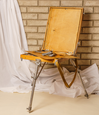 Photo of Artist tool box. Painter's case with portable easel. The sketchbook with palette, paints and brushes on brick backgroundの写真素材