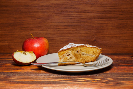 Fresh apples and a piece of apple pie sprinkled with powdered sugar on the background of dark board.の写真素材