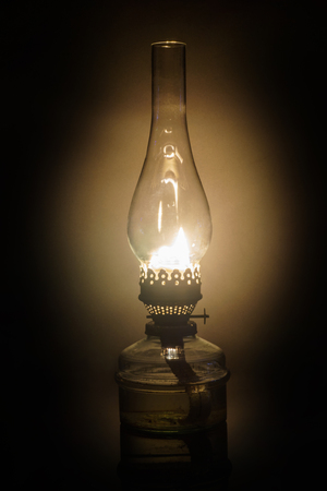 Glowing antique old kerosene oil lamp with vintage glass chimney over the fuel container isolated on blackの写真素材