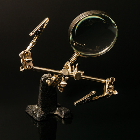 The third hand device with clamps and magnifier for holding small parts during soldering on black background.の写真素材