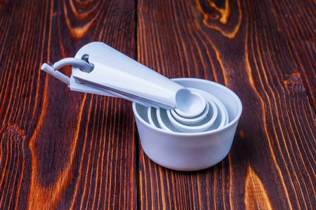 Measuring set table spoons and cups plastic white color on a wooden background. Devices, measuring ingredients for cooking preparationの写真素材