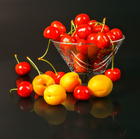 Ripe fresh apricots and cherries in a transparent glass vase on a dark backgroundの写真素材