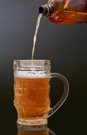 Pouring beer from a PET bottle into a glass mug on a dark background.の写真素材