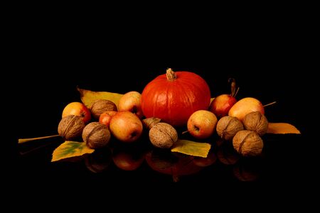 Ripe Hokkaido pumpkin, walnuts and ripe wild apples with yellow autumn leaves isolated on black background.の写真素材