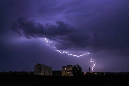 Lightning in big cloud over night city. Black stormy backdrop. Thunderstorm weather. Sky clouds. Dark dramatic scene. Night thunder-storm.の写真素材