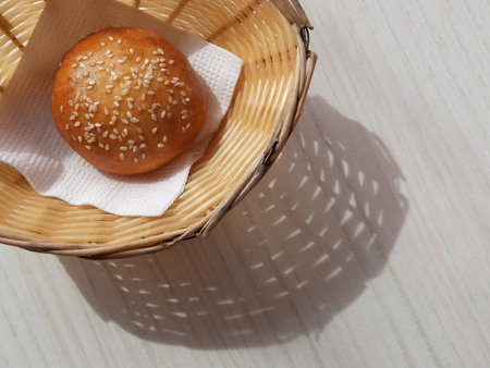 Sunny Breadbasket with long shadow on white wooden table top view. Closeup Bun in basket modern...