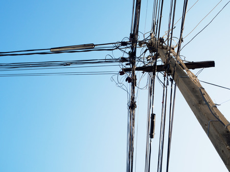 Electric pole and tangled electric cables with blue skyの写真素材
