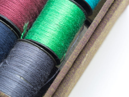 The colorful thread consists of orange, yellow, pink and green in a brown fabric box. On a white...