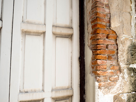 Old wall broken brick  see a orange brickwall inside. The side has old gray wooden doors.の写真素材