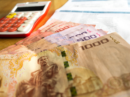 The red calculator and bank note is placed on a wooden table .After calculating the bill of payment.の写真素材