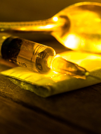 A cocaine injection needle was placed on a wooden table with a cocaine bag and a spoon of light shining down from the cocaine.の写真素材