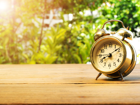 Vintage alarm clock on wood table. The background is green from tree and light bokeh