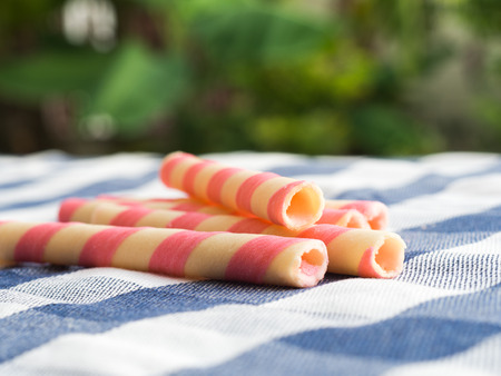pink striped wafer rolls on blue plaid tablecloth. The background is green from tree and light bokehの写真素材