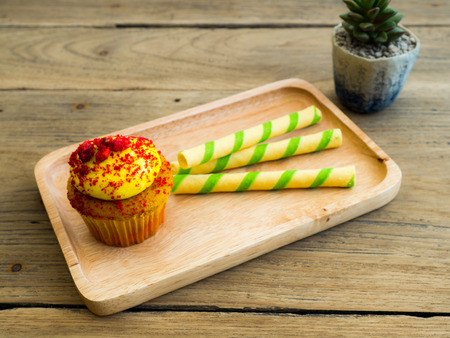 Yellow cupcakes put on wooden plates along with green striped wafer. Beside of cupcake have cactus on the wood tableの写真素材