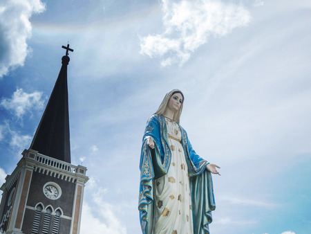 The Blessed Virgin Mary Statue blue sky background. and behind the Virgin Mary, there are temples and crosses. On the sky there Sun haloの写真素材