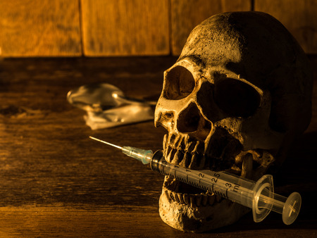 Skull placed on wooden boards. And skull injection syringe The back is medicine Candlelight from the side and a wooden background.の写真素材