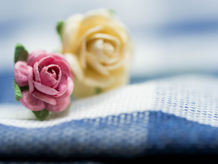 Select focus at pink artificial flowers. pink and yellow artificial flowers made of paper and placed on blue cloth stripes. Green artificial leaves are around artificial flowers.の写真素材