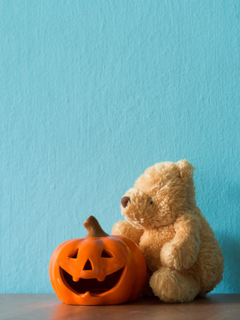 The bear sitting beside of Halloween pumpkin head jack lantern on the wooden table. the background is blueの写真素材
